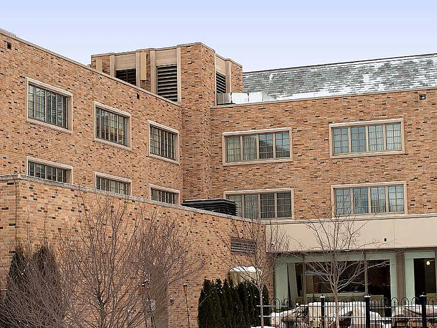 The older wing seen from the courtyard in 2019, three storeys of tan and brown brick over a glazed ground floor, with snow on the roof slope behind
