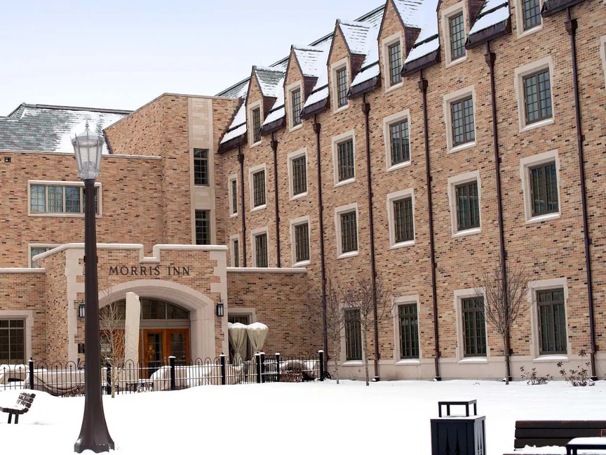 The entrance in 2019 across a snow-covered forecourt, MORRIS INN lettered in the stone over the arch and a lamp standard in front of the dormered range