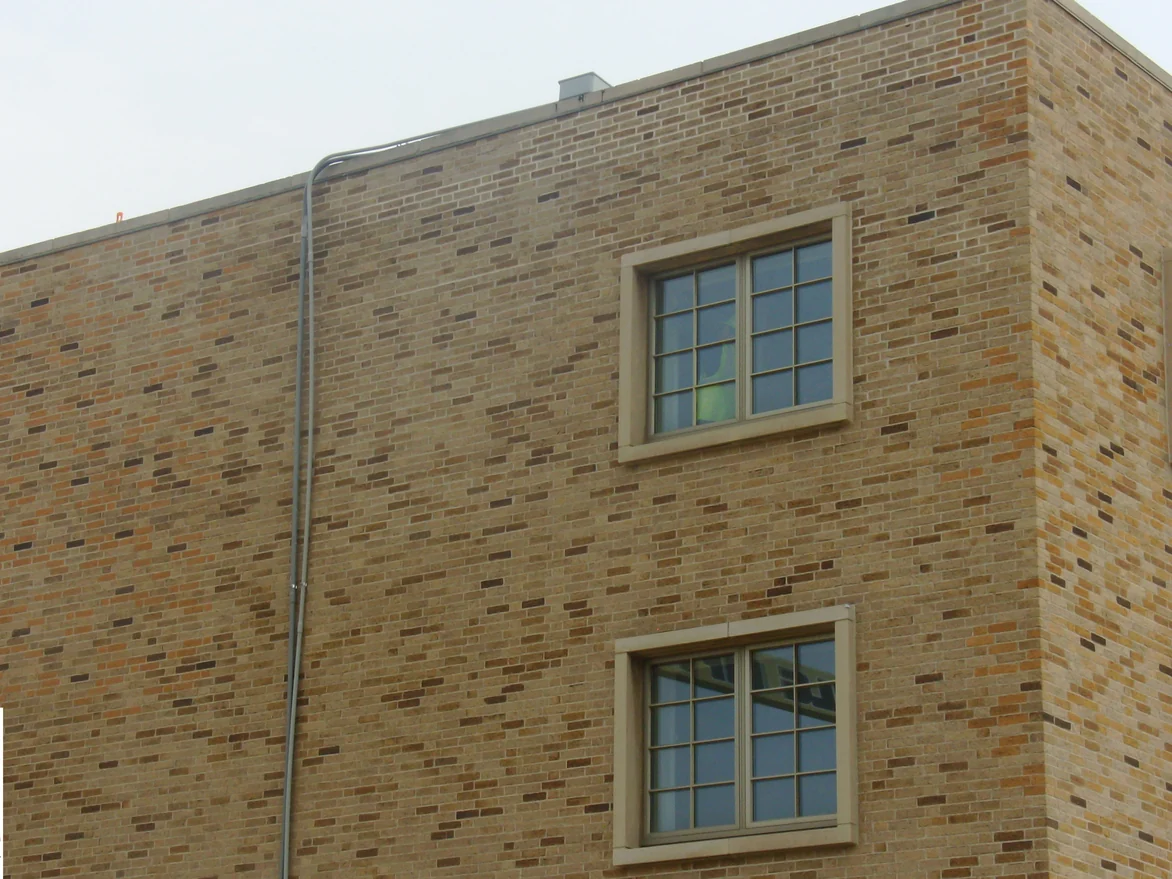 An outside corner of the flat-roofed block in 2010, the brick a light yellow buff with cast stone window surrounds and a downpipe running the full height