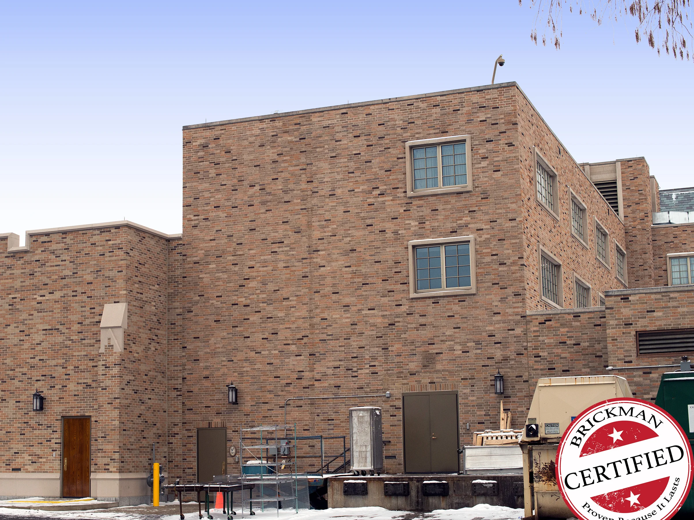 The flat-roofed block in 2019 from the service yard, its brick a mixed range of buff, tan and dark units running across the blank wall and past the window bays