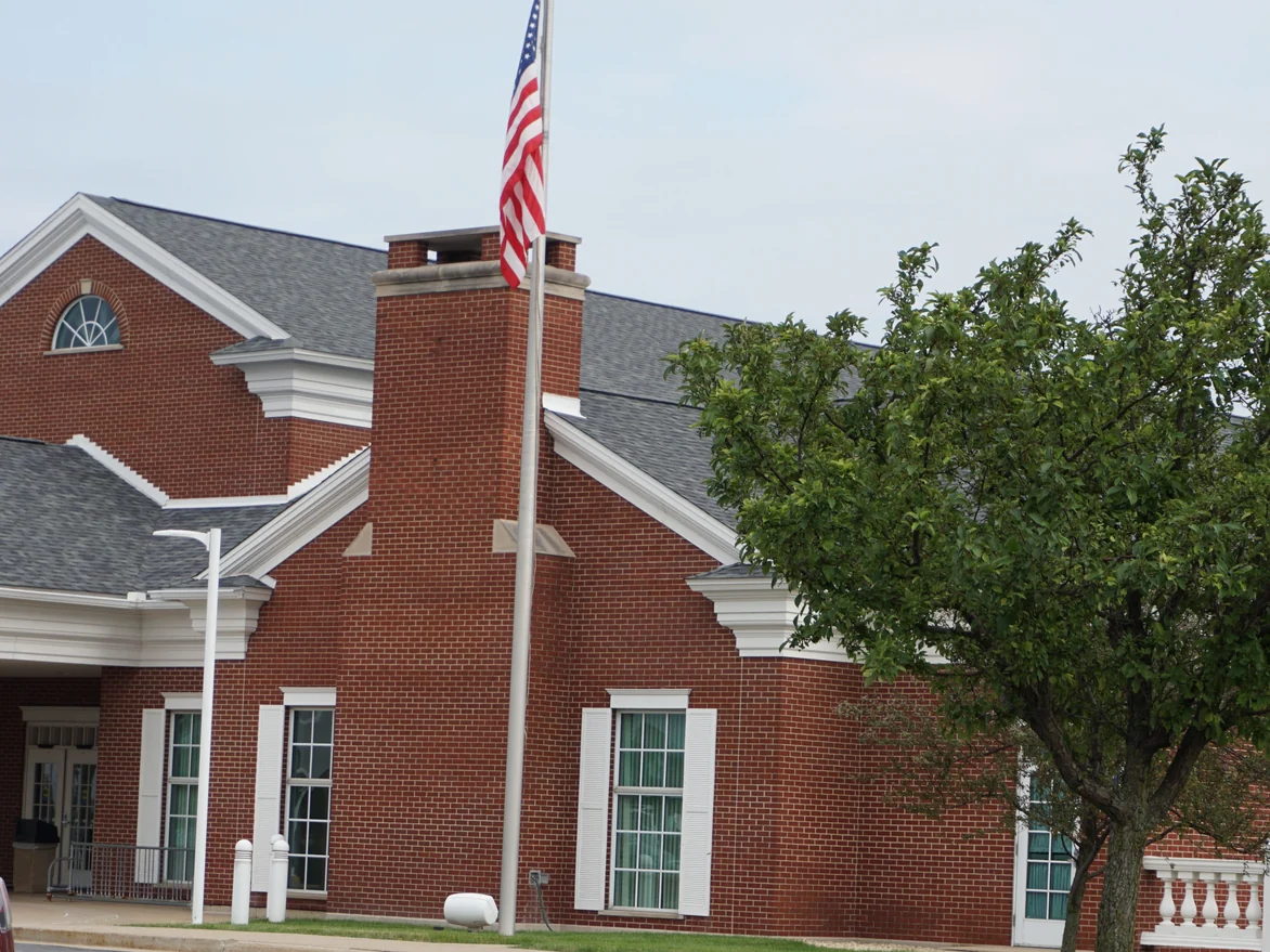 The entrance end of the hospital in 2019, brick running past shuttered windows and a chimney to a flagpole and a covered doorway