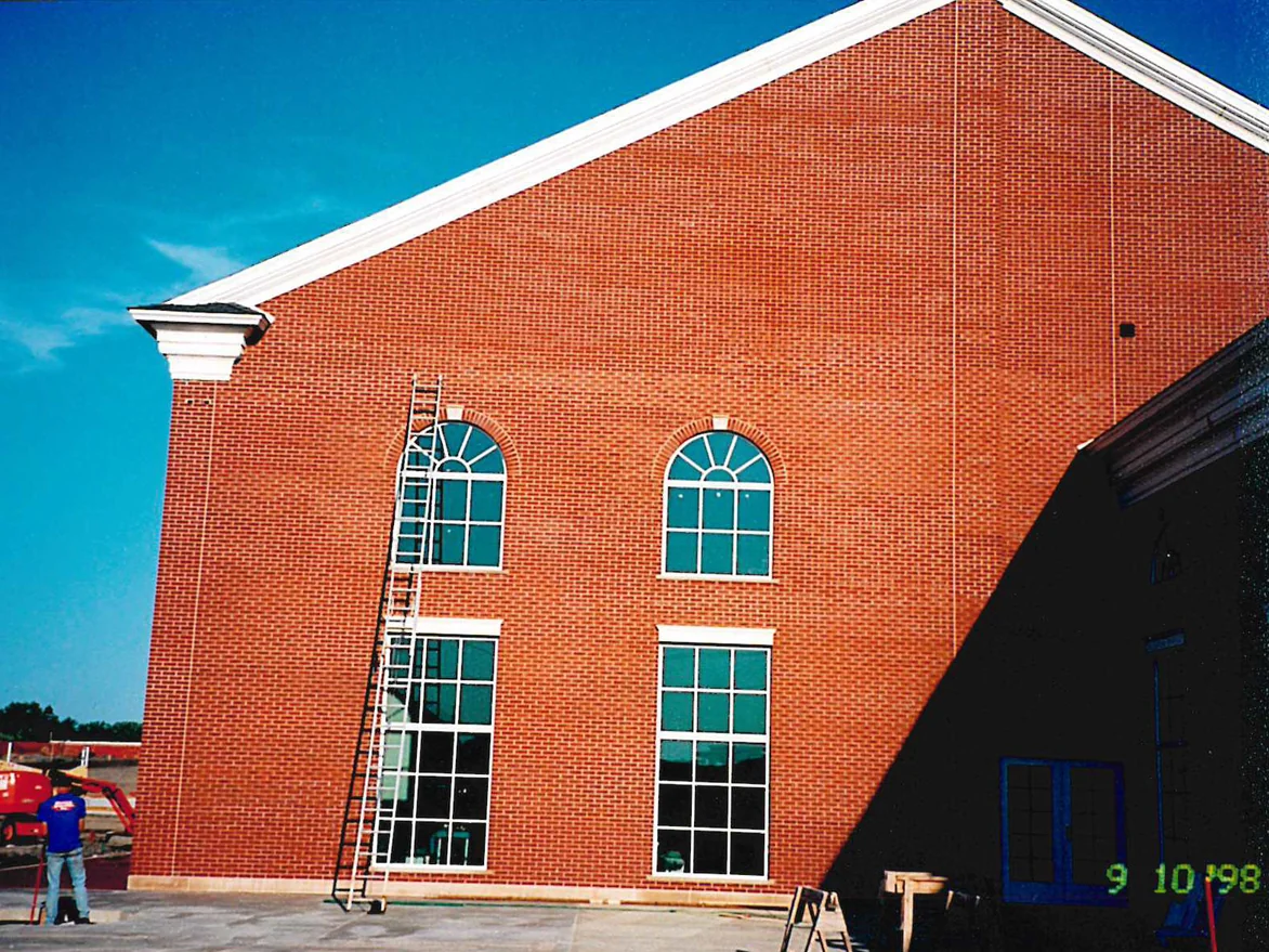 The gable end of the hospital in September 1998 with a ladder up to the second storey, a worker on the ground and a lift parked on the fill beside him