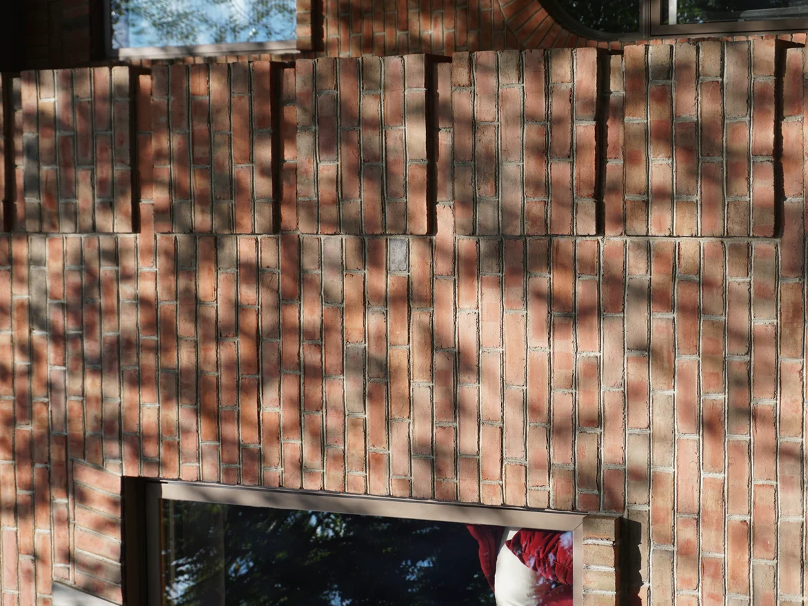 Close view of the brick in 2019 between two windows, bands of upright units running through orange, buff and dark brown with pale mortar joints