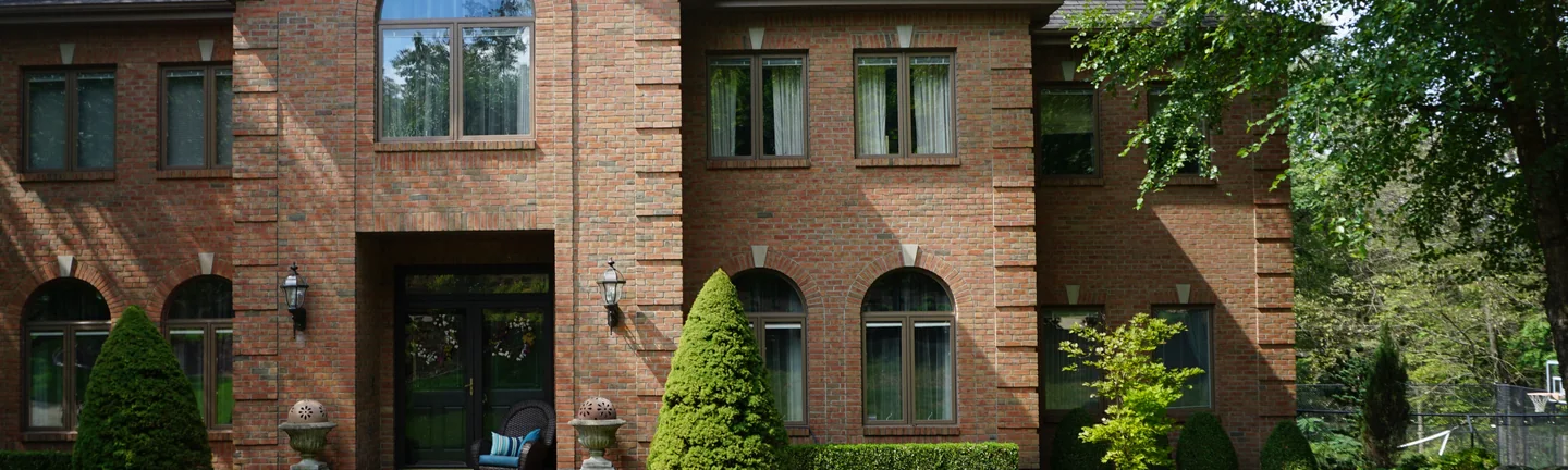The brick front of a two-story home in 2019, an even orange and red range running across the entry and the window bays