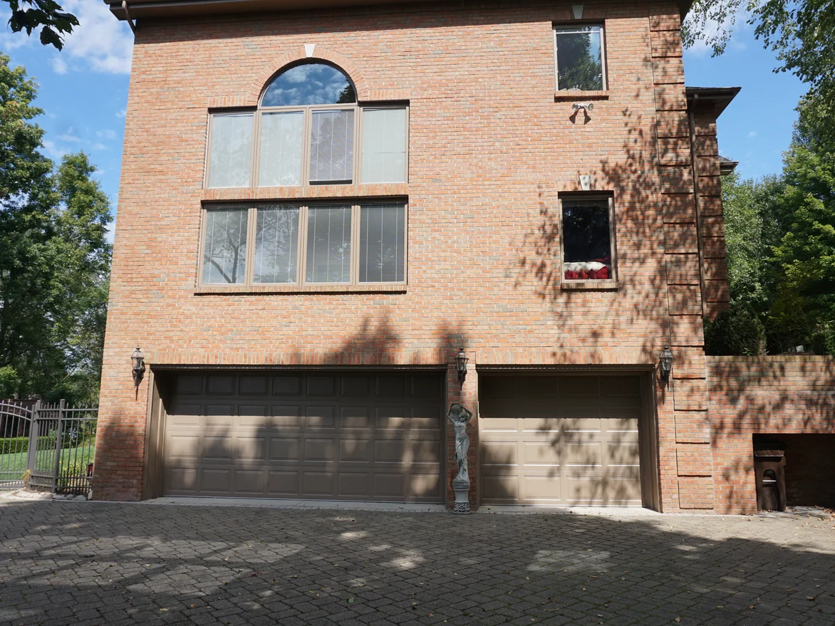 The garage end of the house above its paved drive in 2019, three storeys of brick carrying one even range up to the arched window