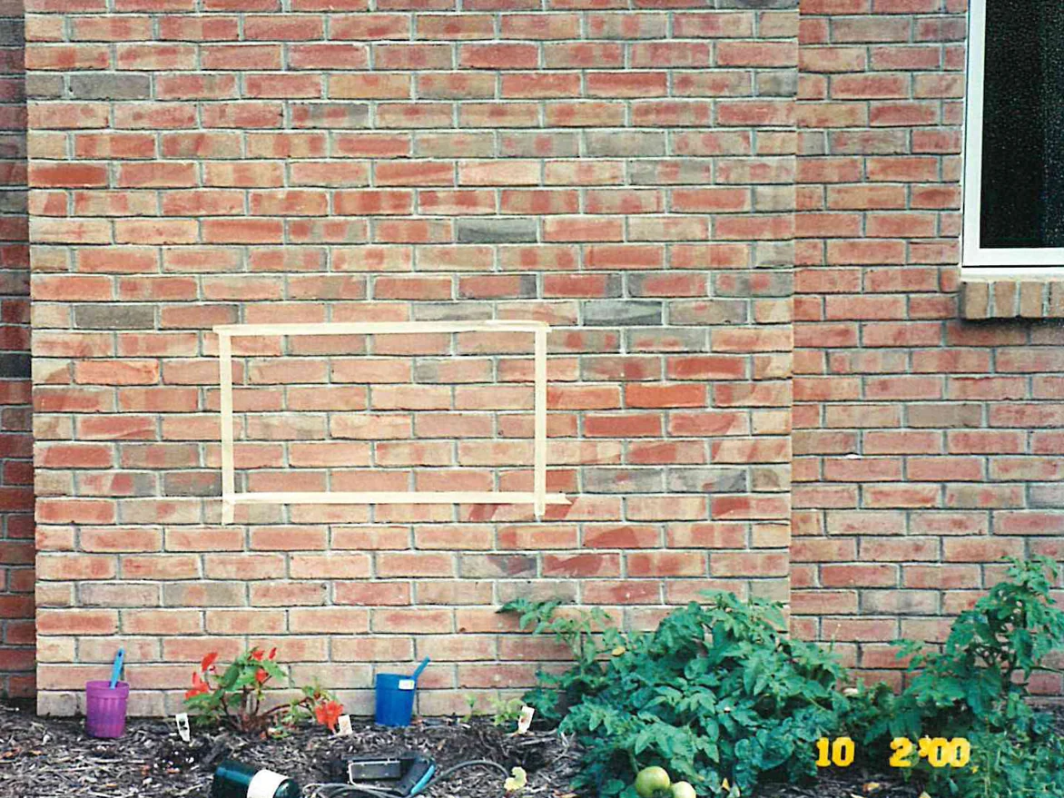A rectangle masked off with tape on the brick wall of the house in 2000, the brick around it blotched pale pink and grey where it had been washed