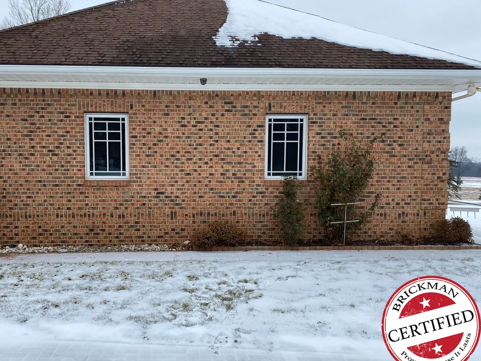 The side elevation of the Nashville, Michigan home in 2021, one range of brick across both windows under a snow-covered hip roof