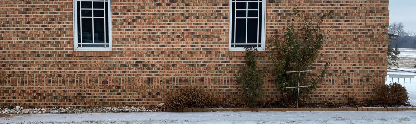 The side elevation of the Nashville, Michigan home in 2021, its brick reading as one range under a snow-covered hip roof