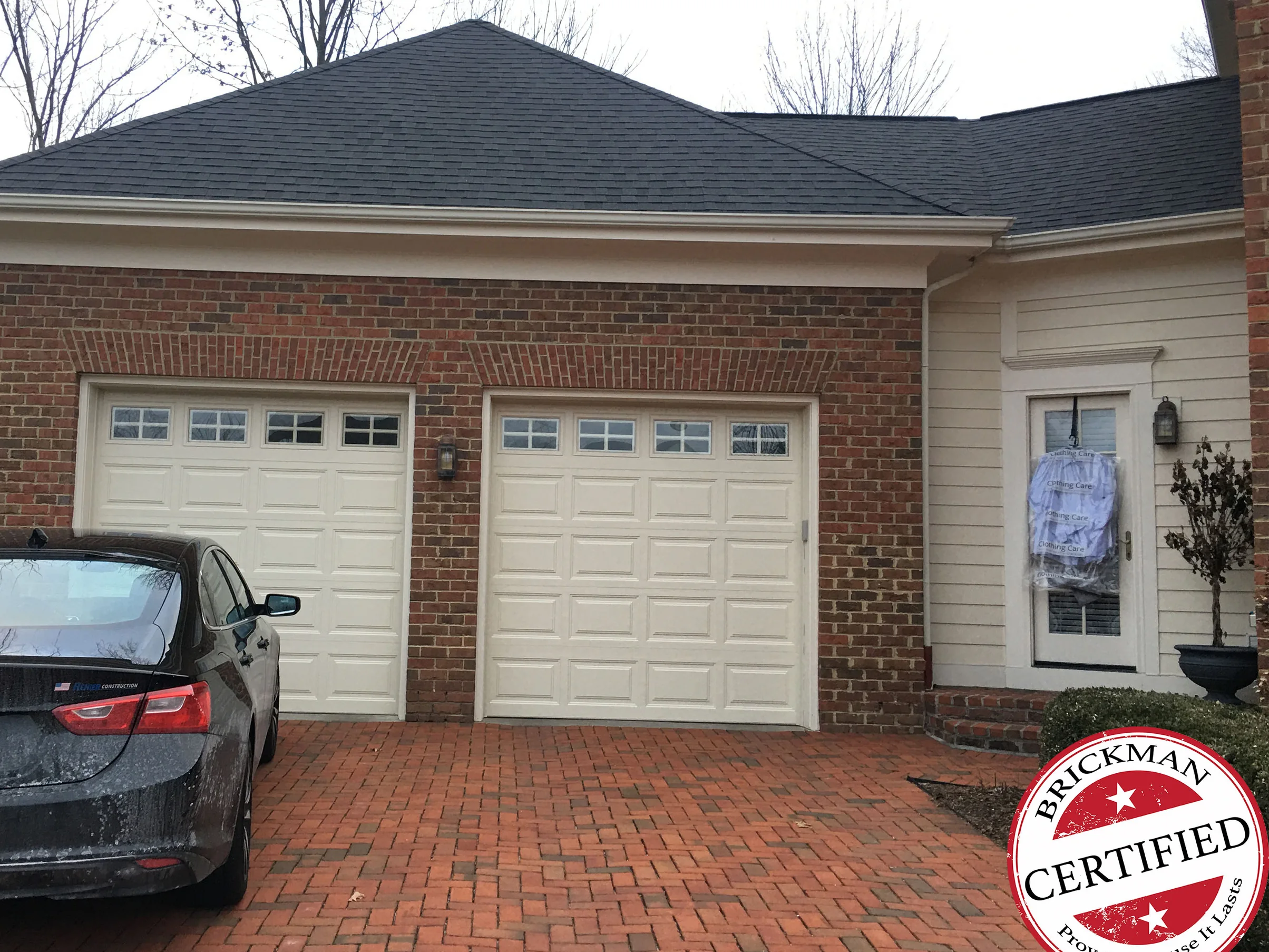 The garage of the New Albany house in 2021, two white doors under a hip roof with the jack arch over each door reading in the same dark red blend as the wall, the certification stamp in the corner
