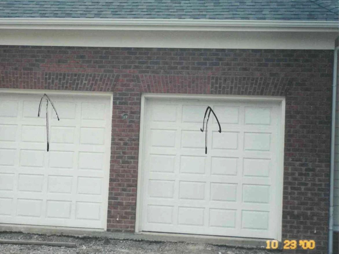 Two garage doors in October 2000, the flat jack arch over each one showing lighter and redder than the dark blended brick around it, with black arrows drawn on the print pointing up at both arches