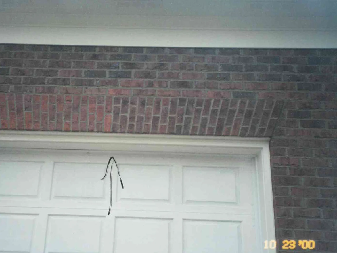 Close view of the jack arch over one garage door in October 2000, its upright units a pinker red than the dark field brick above and beside it, an arrow drawn on the print pointing up at the arch
