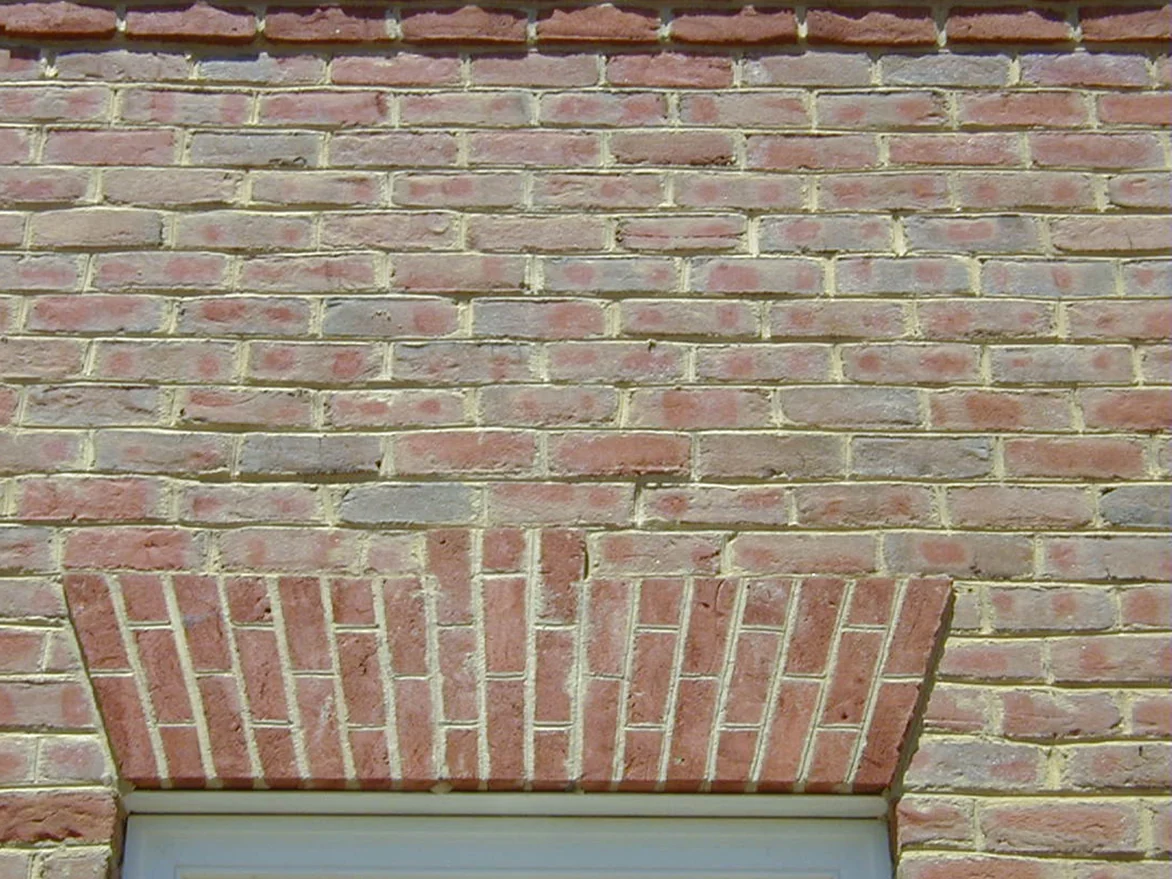 A brick jack arch over a window after staining, the angled units now a deeper red that separates the arch from the field brick