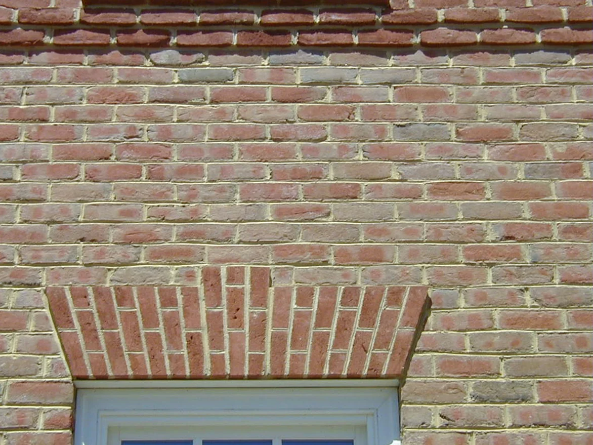 A brick jack arch over a window before staining, its angled units reading much the same warm orange as the wall around them