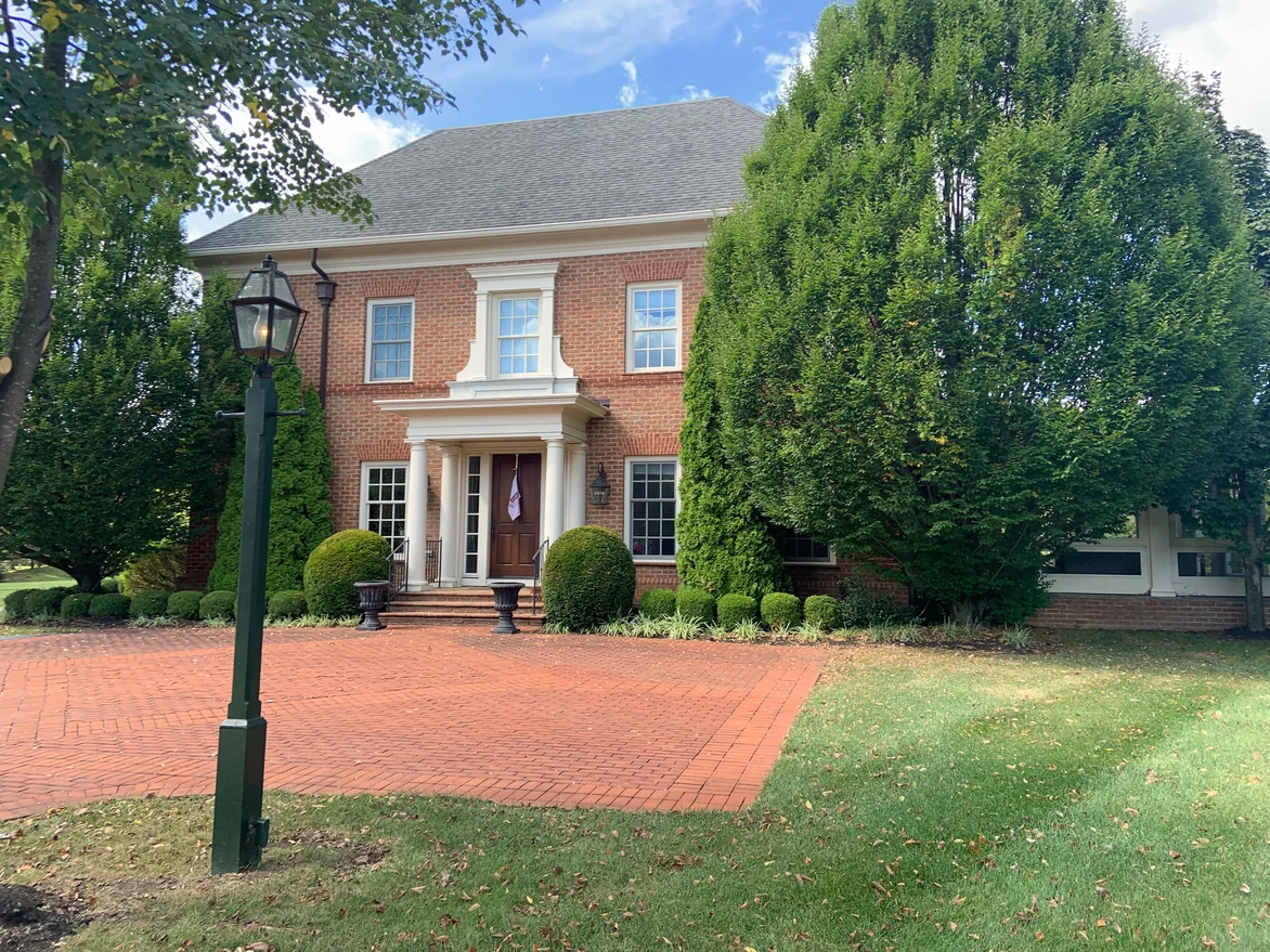 The house seen across its brick motor court in 2019, with a gas lamp post in the foreground and clipped hedges along the front