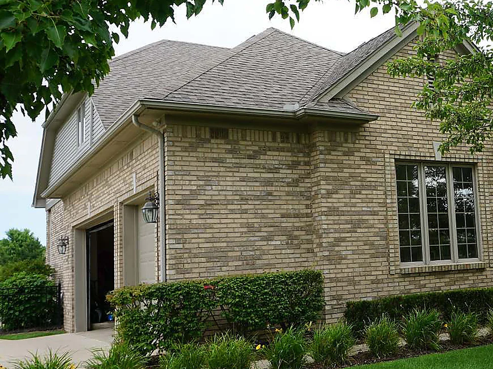 The garage-side corner of the New Baltimore house in 2019 under a mature tree, the brick one even tan and buff blend from the garage door to the gable