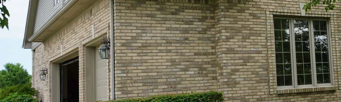 The brick of the New Baltimore house in 2019, one tan and buff blend running from the garage door past the tall window