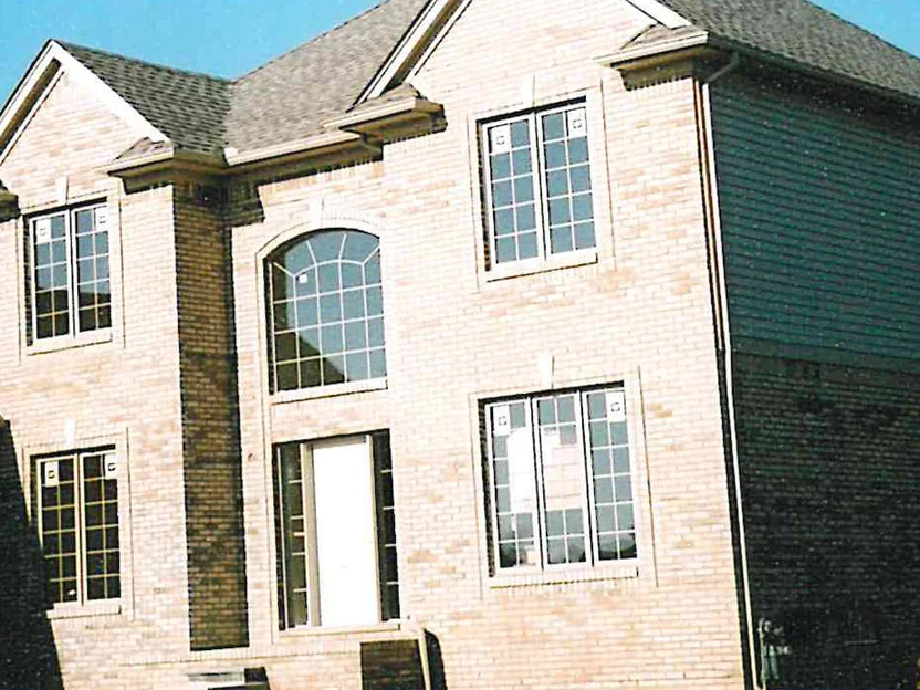 The entry gable and the arched window over the door in November 2003, dark units scattered through the pale brick and the sided upper wall of the garage wing at the right