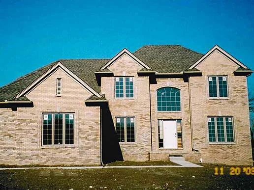 The whole front of the new two-story house on 20 November 2003, three brick gables over a bare dirt lot, the brick a patchy mix of light and dark units under a clear sky