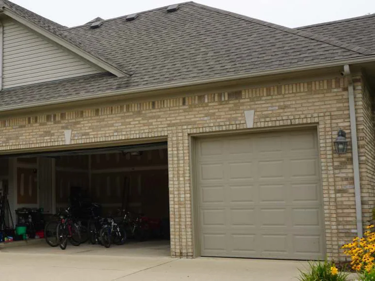 The three-car garage front in 2019, one bay open, the soldier course above the doors and the corners now reading as one blend with the wall