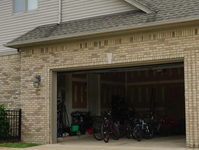 The open garage bay in 2019 with bicycles inside, the brick pier and the wall beside it in the same tan and buff blend as the rest of the house