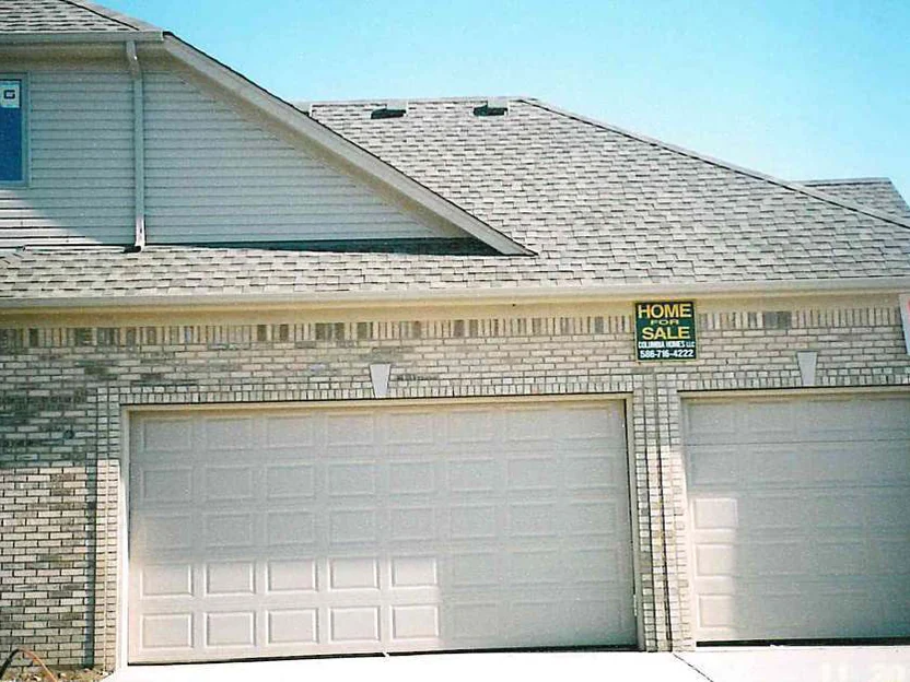 The three-car garage front in November 2003 with a builder's for sale sign on the wall, dark units clustered at the left corner and scattered through the soldier course above the doors