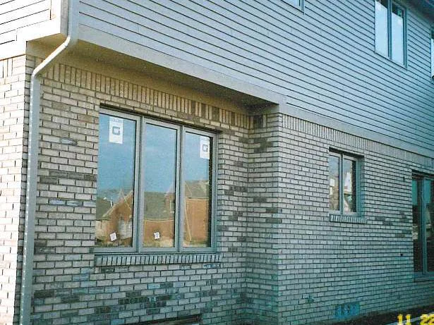 The rear corner in 2019 with a patio set and a grill against the wall, the brick that carried the dark clusters now one even tan range below the siding