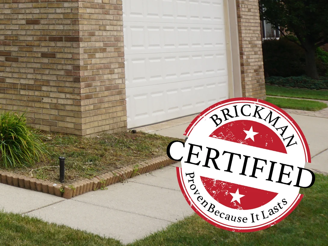 An outside brick corner at ground level in 2019, cream, tan and brown units above a bed edged with brick, the frame carrying the Brickman Certified stamp