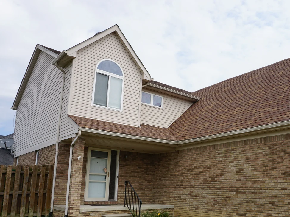 The covered front entry and the long brick wall in 2019, the brick reading as one tan and buff range from the porch to the eaves