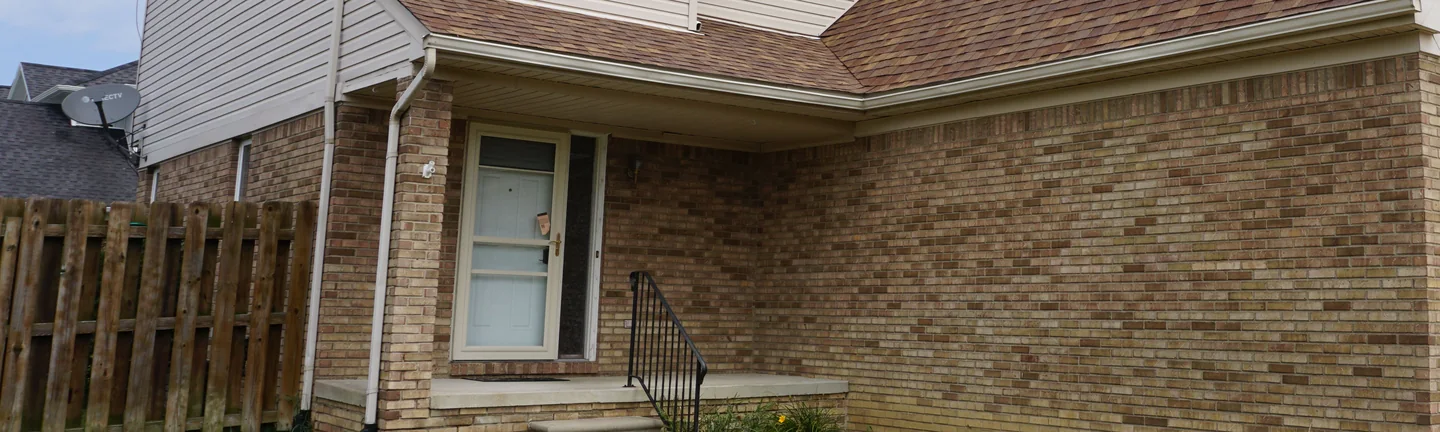 The front of the New Baltimore house in 2019, its blended tan and buff brick running from the entry along the wall