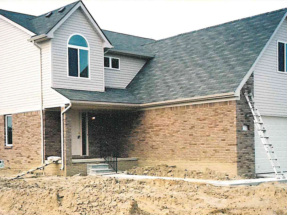 The same house in June 2003, a ladder up the garage gable at the right and the dirt of the unfinished yard banked against the lower courses of brick
