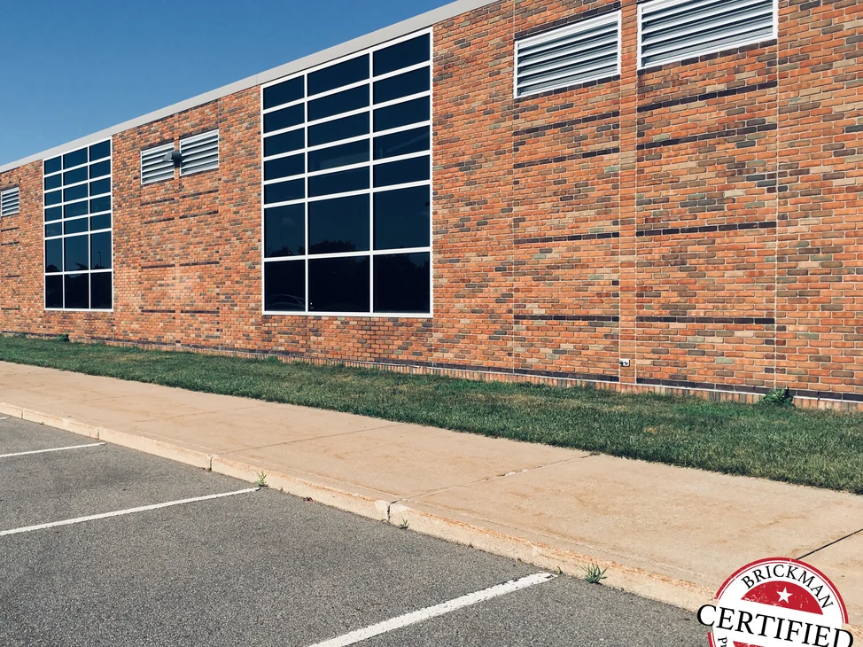The long side of the school in 2019, tall windows set in brick that runs as one range of reds, tans and browns with darker courses banding across it.