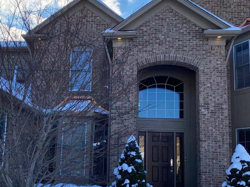The front of the Northville house in 2021 under snow, brown brick reading as one range across the two-storey arched entry