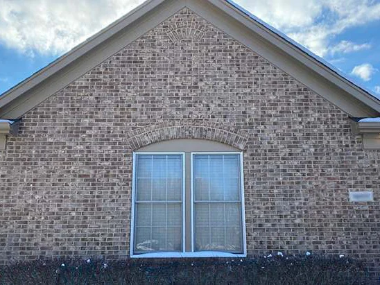 The same gable end in 2021 with finished trim, gutters and a planted hedge below the window, the brick still one range through the arch and the fan detail at the peak