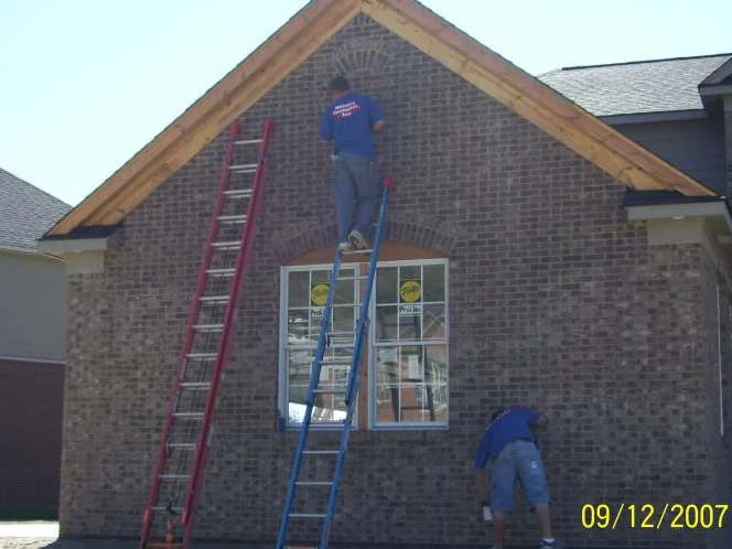Two applicators at the gable in September 2007, one standing on an extension ladder working stain into the brick by hand, the other crouched at the foot of the wall