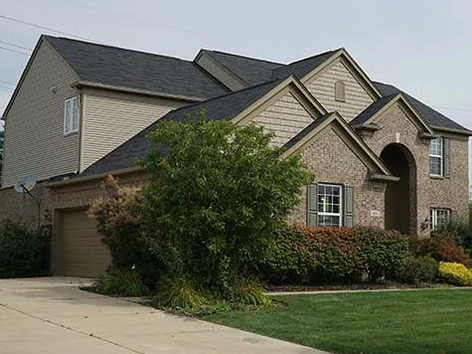 The house from the driveway in 2019, garage on the left, the brick one range past a tree and the front beds to the arched entry