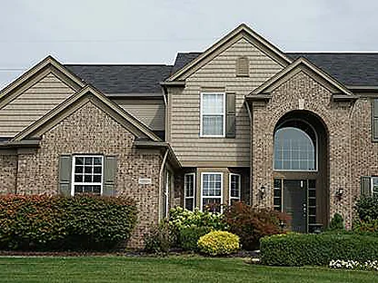 The front of the house in 2019 with shrubs and lawn in, the brick one tan range across the gables and the arched entry