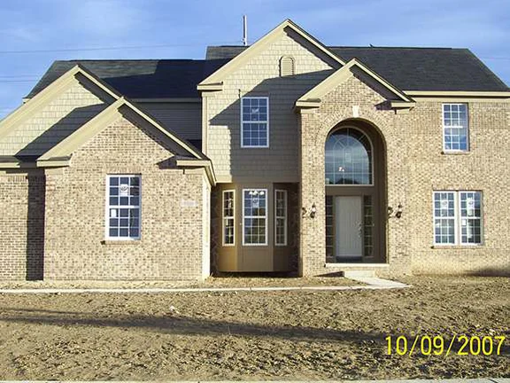 The front of the two-story house in October 2007 before any landscaping, tan brick under vinyl-sided gables with patches of lighter and darker units across the face, and a camera date of 10/09/2007