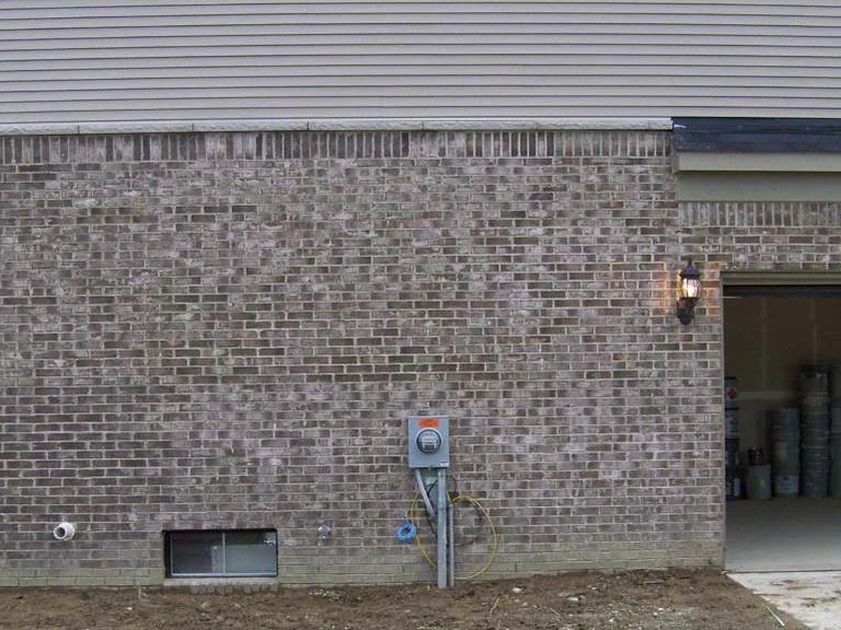 The garage side wall in 2007 with the door up, a meter and hose bib on the brick, and blotches of light and dark units through the courses