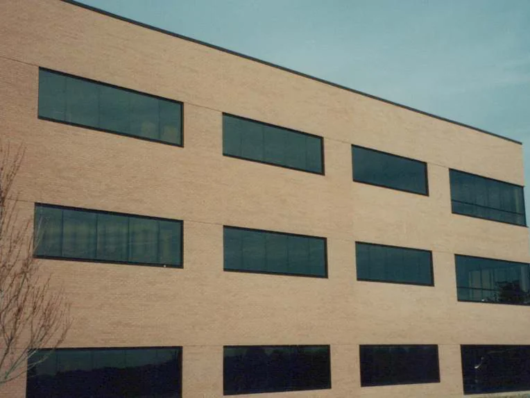 The same elevation in 1999 after the headers were blended, tan brick and three rows of ribbon windows with a bare tree in front and a neighbouring building at the right