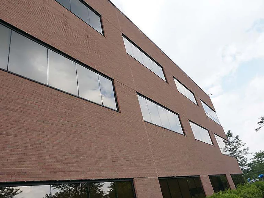 The long elevation of the office in 2019 seen from close to the wall, red brick and three rows of ribbon windows running away to trees at the right