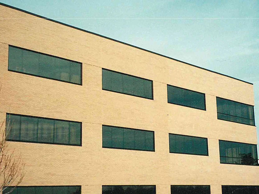 The long elevation of the three-story office in 1999, tan brick and three rows of ribbon windows over bare ground, before staining