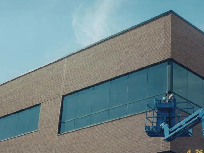 An applicator in a blue boom lift at the top corner of the building in 1999, working the header brick beside the corner window, with a camera date stamp in the lower corner of the frame