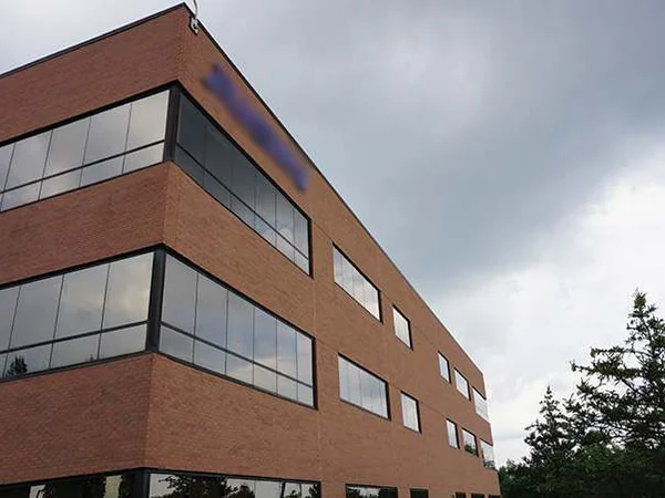 The other corner of the office in 2019 under a stormy sky, a mature pine at the right and the tenant sign on the top floor blurred in the file