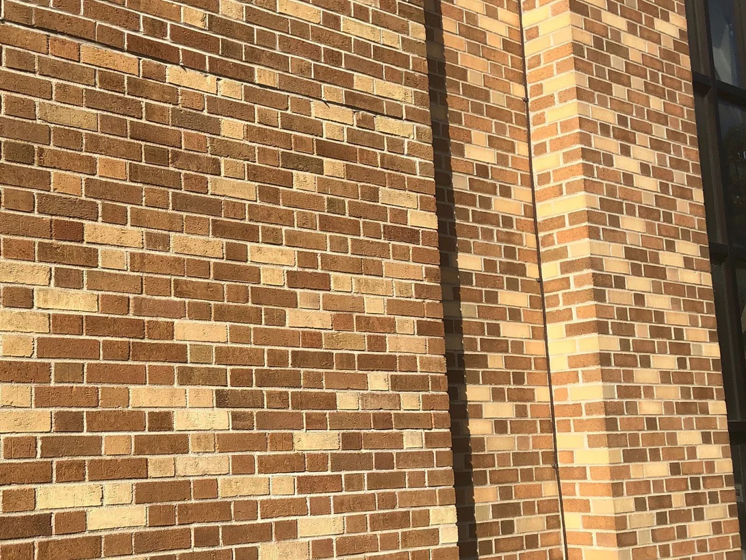 A stained wall in 2019 in raking light, the courses reading as one blend across a downpipe and a window reveal