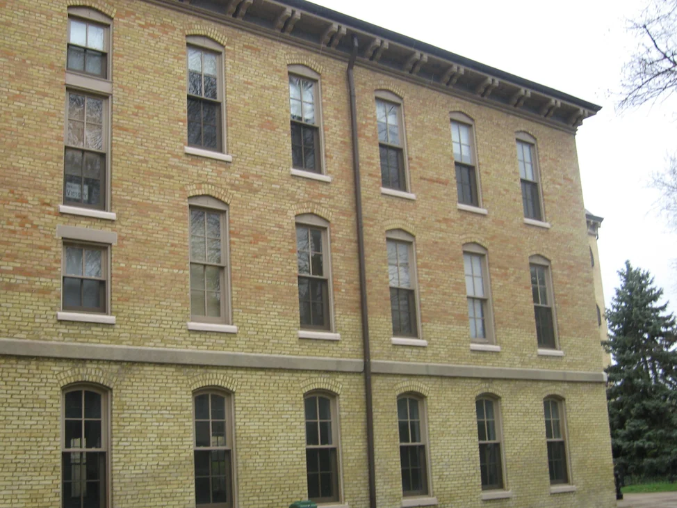 The long side wall of Washington Hall before the work, three floors of pale yellow brick at ground level with the two upper floors running orange and pink above a stone belt course.