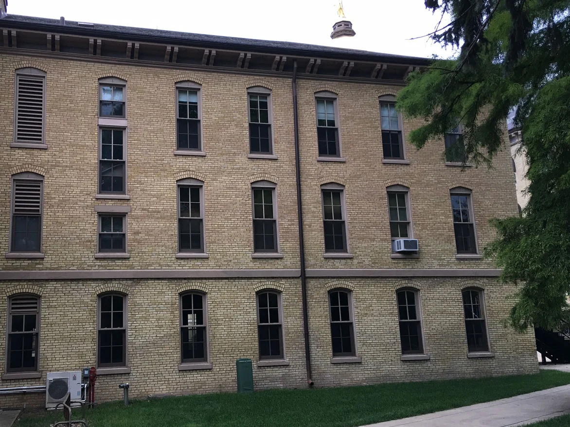 The same elevation after the work, all three floors reading as one buff yellow range, with the gilded statue and lantern of the campus dome standing above the roofline