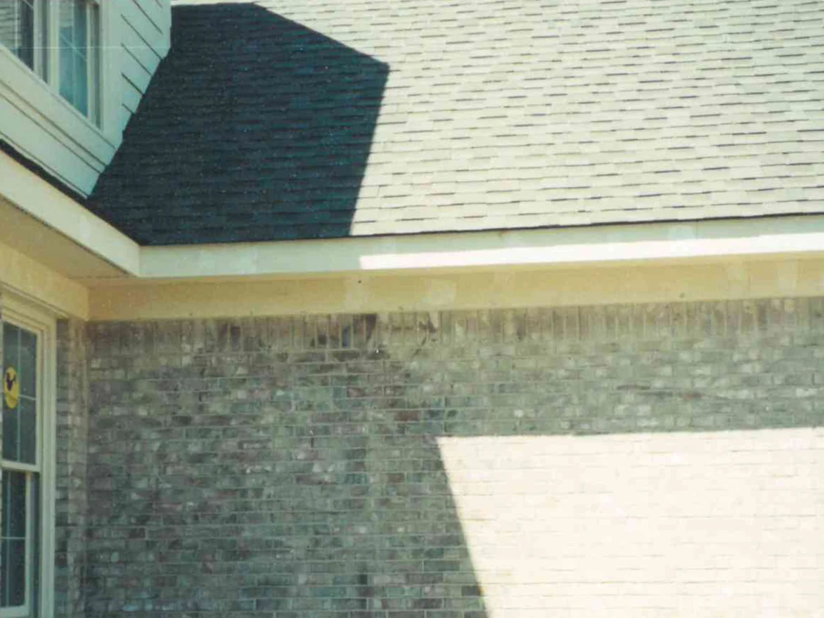 The corner of the house in 1999 before staining, grey and tan brick under a soldier course with a pale washed-out patch and streaks running down the face