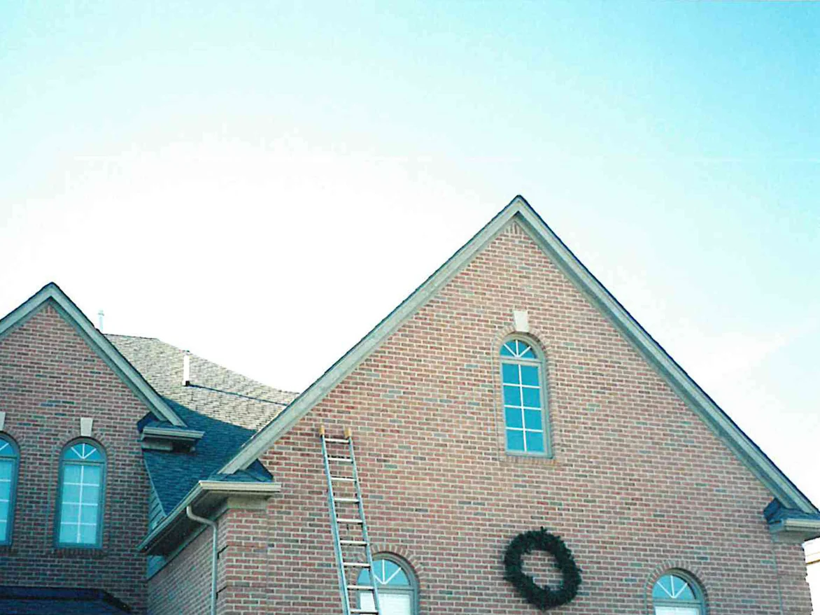 Two gables of the house in 1998 with a ladder still standing against the wall, the brick reading as one red and tan range across both of them