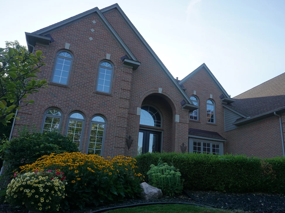 The front of the house in 2019 from the garden, the brick holding one red and tan range across the tall gable, the arched entry and the wing beyond