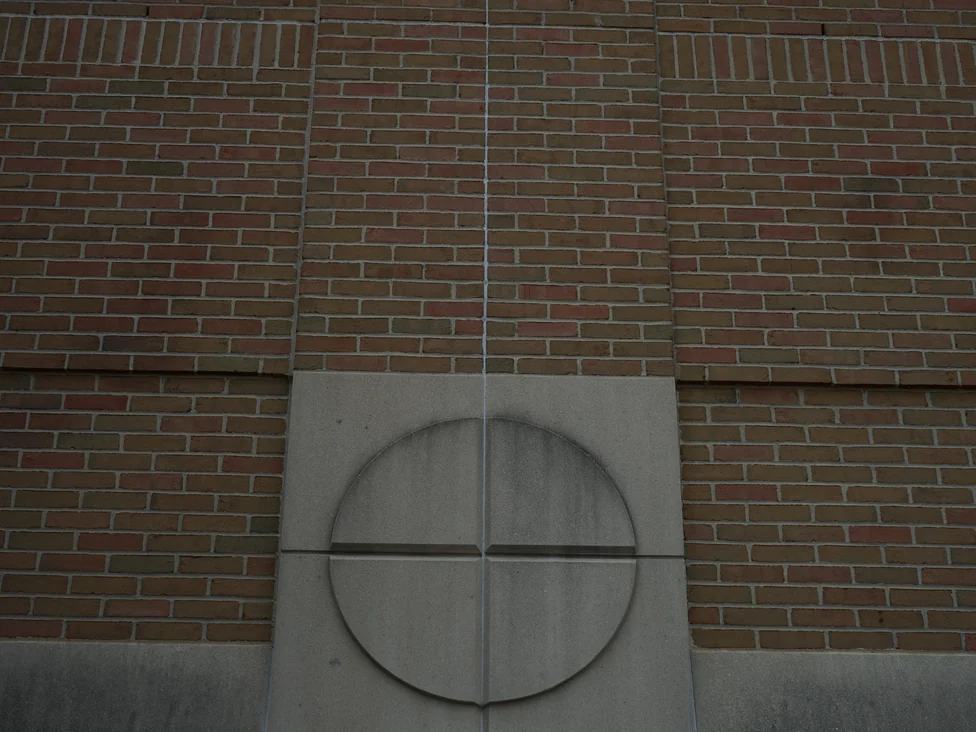 Close view of the brick in 2019 either side of a cream precast panel with an incised circle, the courses running red, tan and buff with no group of one color